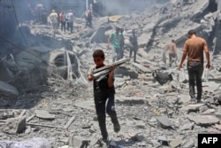 Dječak nosi predmete spašene iz ruševina zgrade uništene tokom izraelskog bombardiranja izbjegličkog kampa al-Shati u gradu Gaza 22. juna 2024. godine, usred sukoba između Izraela i palestinske militantne grupe Hamas.