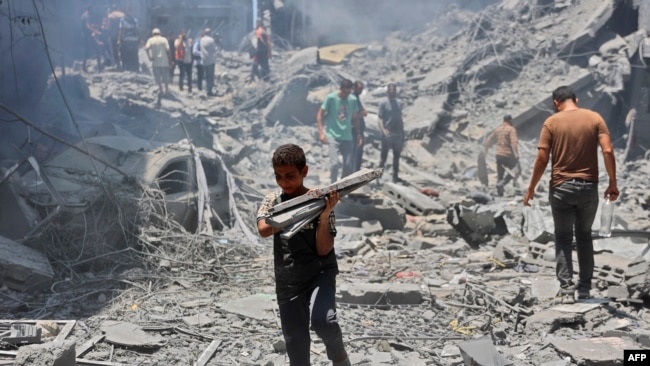 Një djalë mban sende që ka gjetur në rrënojat e një ndërtese të shkatërruar gjatë sulmeve izraelite në kampin e refugjatëve al-Shati në qytetin e Gazës më 22 qershor 2024, ndërsa vazhdon konflikti mes Izraelit dhe grupit militant palestinez Hamas.
