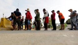 FILE - Migrants seeking asylum in the United States line up for a meal provided by volunteers near the international bridge in Matamoros, Mexico, April 30, 2019.