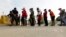 FILE - Migrants seeking asylum in the United States line up for a meal provided by volunteers near the international bridge in Matamoros, Mexico, April 30, 2019. 