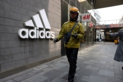 A delivery man walks past an Adidas store and an H&amp;M store in Beijing on March 25, 2021.