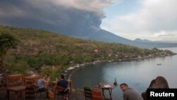 Para wisatawan menyaksikan letusan Gunung Agung dari sebuah restoran di Pantai Jemeluk, Amed, Karangasem, Bali, 26 November 2017. (Antara Foto/Nyoman Budhiana/ via REUTERS)