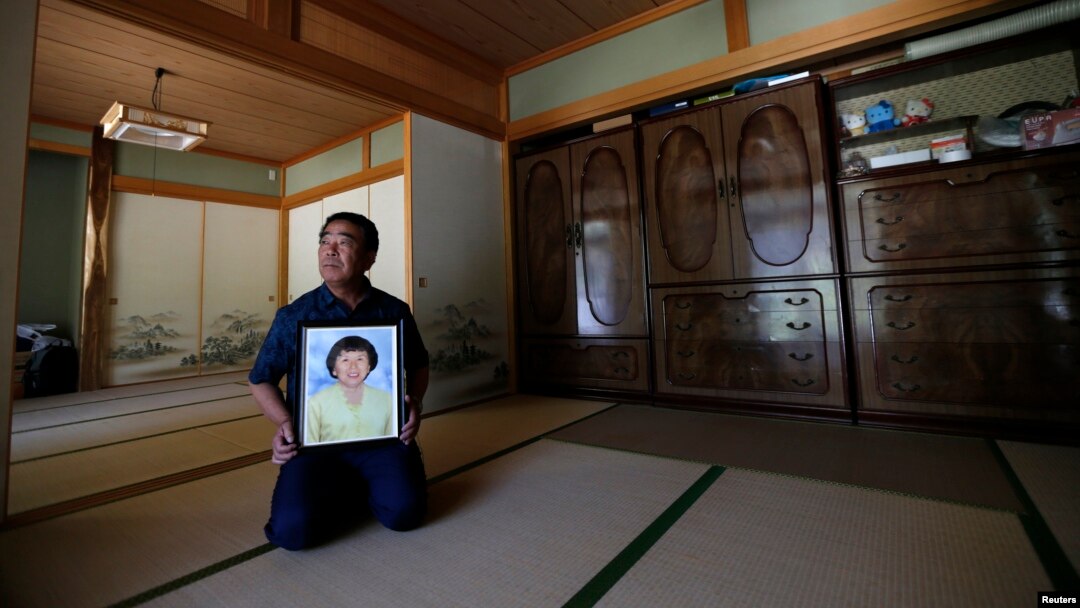 FILE - Mikio Watanabe holds a portrait of his late wife Hamako at his home at Yamakiya district in Kawamata town, Fukushima prefecture, June 23, 2014.