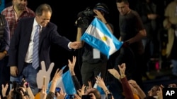 FILE - Ruling party presidential candidate Daniel Scioli holds an Argentine flag as he acknowledges supporters after primary elections in Buenos Aires, Argentina, Aug. 10, 2015.