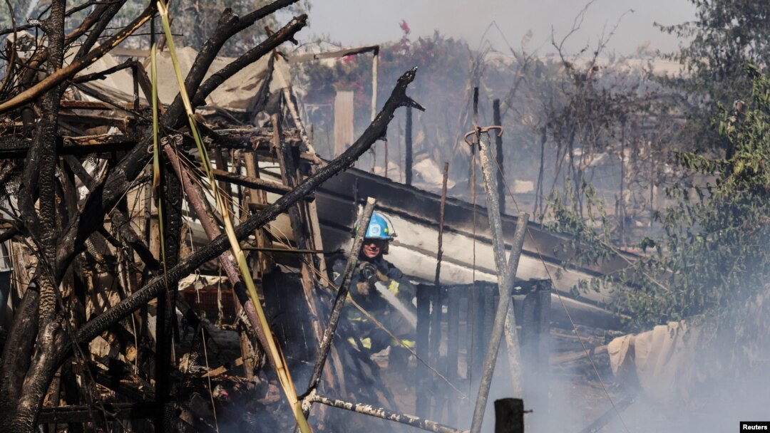 A firefighter extinguishes a blaze at the scene where a rocket launched from the Gaza Strip landed, causing fatalities, on a farm just over the Gaza border, in Moshav Ohad, southern Israel, May 18, 2021.
