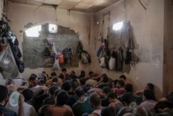 FILE - More than 100 Islamic State suspects sit inside a small room in a prison south of Mosul, July 18, 2017.