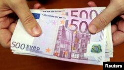 FILE - A bank employee holds a pile of 500 euro notes at a bank branch in Madrid, Jan. 13, 2011. 