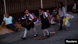 School girls walk past migrants waiting in line to enter the Mexican Comission for Refugee Assistance (COMAR) in Tapachula, Mexico, May 13, 2019.
