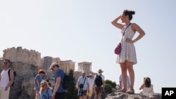 Turistas de pie en la colina de Aerópago ante la antigua Acrópolis, en el centro de Atenas, el miércoles 12 de junio de 2024. 