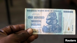 FILE - A man holds up for a picture a one hundred trillion Zimbabwean dollars note inside a shop in Harare, Zimbawe.