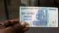 FILE - A man holds up for a picture a one hundred trillion Zimbabwean dollars note inside a shop in Harare, Zimbawe.