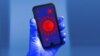 ILUSTRACIJA - Model koronavirusa na ekranu mobilnog telefona, koji drži ruka u rukavici 