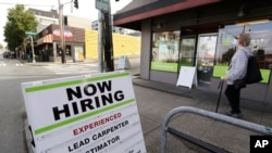 In this photo taken Thursday, June 4, 2020, a pedestrian wearing a mask walks past reader board advertising a job opening for a remodeling company, in Seattle. 