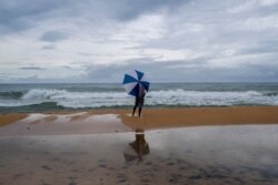 Un hombre bajo una sombrilla observa las olas que golpean en la playa mientras la tormenta tropical Laura pasa sobre San Juan, Puerto Rico, el 22 de agosto de 2020