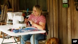 In this April 11, 2020, photo, Cathia Schmarje sews a face mask on the front porch of her home in Liberty County, Florida, that became the last county without a case
