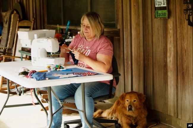 In this April 11, 2020, photo, Cathia Schmarje sews a face mask on the front porch of her home in Liberty County, Florida. She's sewn masks for her son and his employees, and she'll give some to townsfolk who need one. (AP photo)