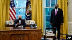 拜登總統在白宮橢圓形辦公室簽署取消不許跨性別者參軍的禁令，國防部長奧斯汀站立在一旁。(2021年1月25日)
