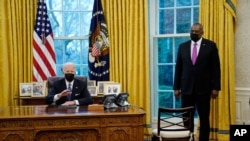 Secretary of Defense Lloyd Austin listens as President Joe Biden speaks before signing an Executive Order reversing the Trump era ban on transgender people serving in the military, in the Oval Office of the White House, Jan. 25, 2021.