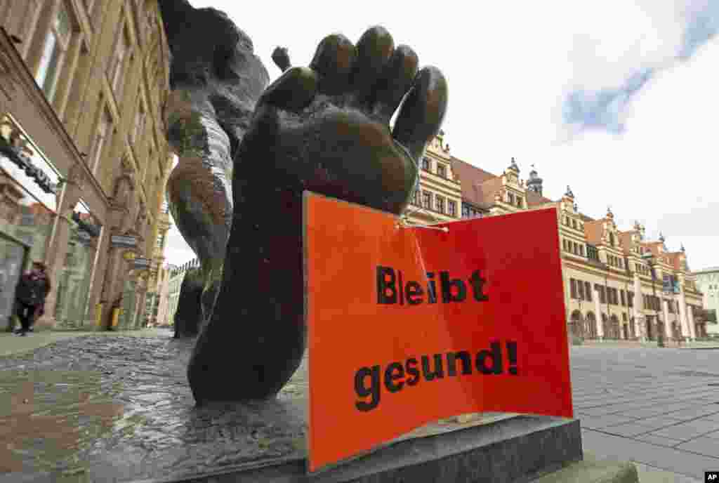 Un letrero que dice "Manténgase saludable" cuelga de la escultura "El paso del siglo", de Wolfgang Mattheuer, en Leipzig, Alemania.