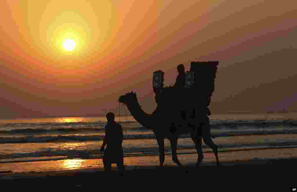 A Pakistani rides a camel on a beach during the last sunset of 2018, in Karachi, Dec. 31, 2018. 