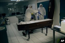 Workers in full protective gear disinfect the casket of a coronavirus victim at the Fontaine funeral home during a partial lockdown to prevent the spread of the disease in Charleroi, Belgium, April 15, 2020.