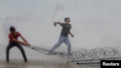 A protester supporting the opposition Cambodia National Rescue Party (CNRP) throws a stone as another tries to remove barbed wire barricades during clashes with police officers near the Royal Palace in central Phnom Penh Sep. 15, 2013.