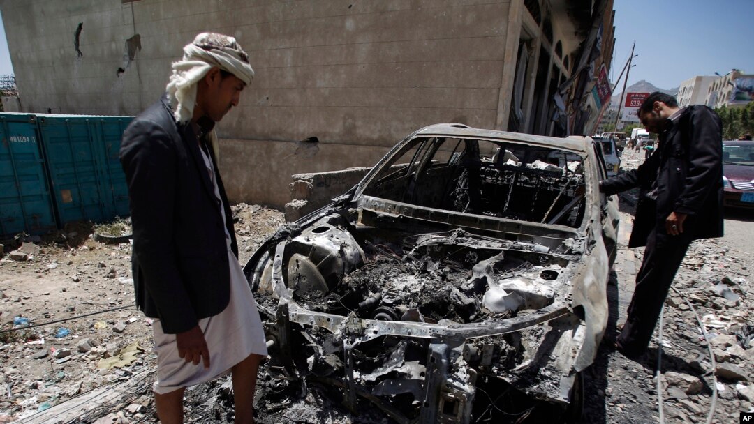 Para pria memperhatikan sebuah mobil yang hancur akibat serangan udara yang dipimpin oleh Arab Saudi di ibukota Yaman, Sana'a, Sabtu, 25 April 2015. (AP Photo/Hani Mohammed)