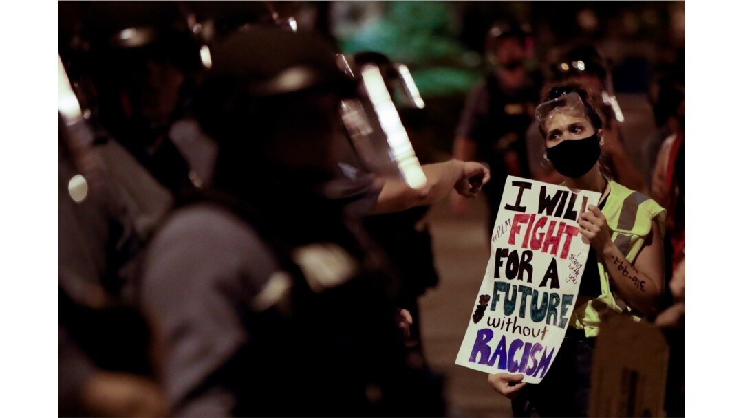 FILE - A protester confronts a line of police in riot gear after a unity march to protest police brutality, in Kansas City, Mo., June 4, 2020.