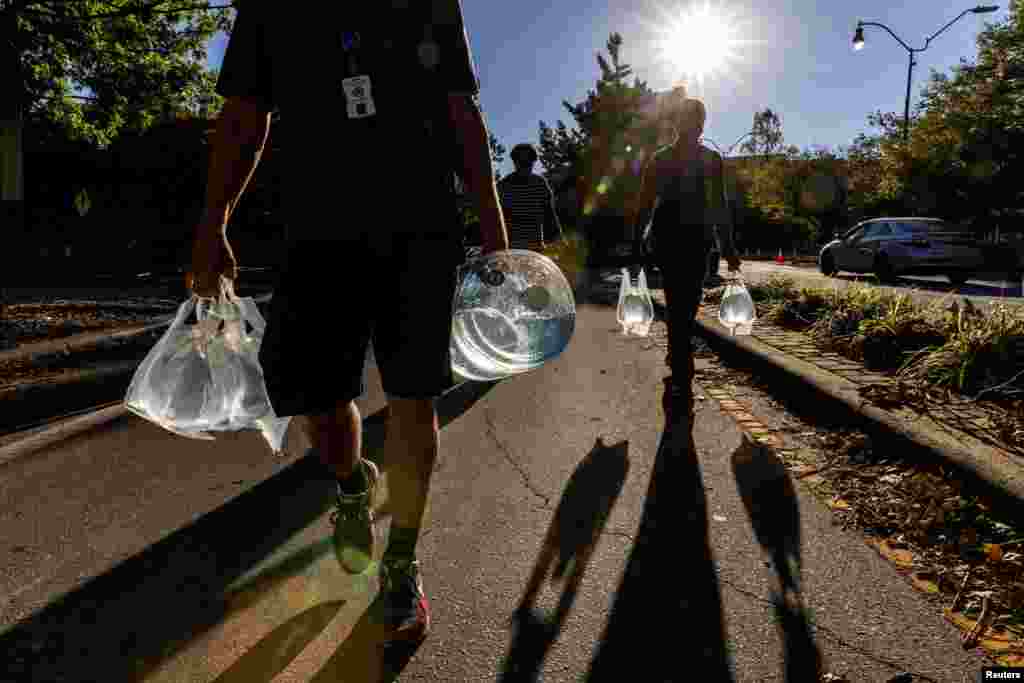 People walk with water collected from a truck following the passing of Hurricane Helene, in Asheville, North Carolina, Oct. 2, 2024. 