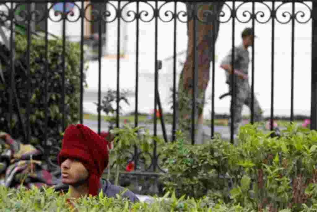 An anti-government protester sits behind a bush as an Egyptian soldier walks in the background, outside the Egyptian Parliament in Cairo, Egypt, Wednesday, Feb. 9, 2011. Around 2,000 protesters waved huge flags outside the parliament, several blocks from 