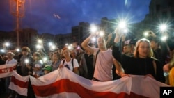 Belarusian opposition supporters, with their phone flashlights lit, hold old Belarusian national flags during a rally protesting election results, in front of a government building at Independence Square, in Minsk, Belarus, Aug. 20, 2020.