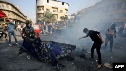 Iraqi demonstrators grapple with a tear gas canister during clashes with security forces in the capital Baghdad's al-Rasheed street near al-Ahrar bridge, Nov. 26, 2019.