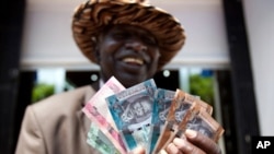 A South Sudanese man poses with a fistful of South Sudanese Pounds. A high-level minister says the government is planning to ban unofficial trading in U.S. dollars.