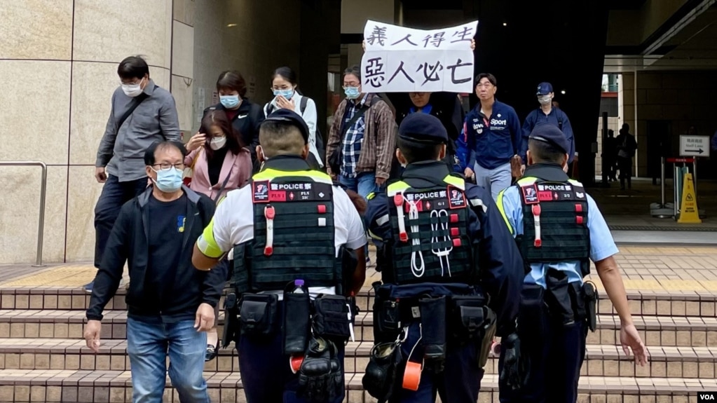 2024年11月19日，香港民主派初选案被告吕智恒的养母Elsa在吕智恒被判刑后，在西九龙裁判法院大楼外高举”义人得生、恶人必亡”的标语。她立即被多名香港警员包围及带上警车。 (美国之音照片) 