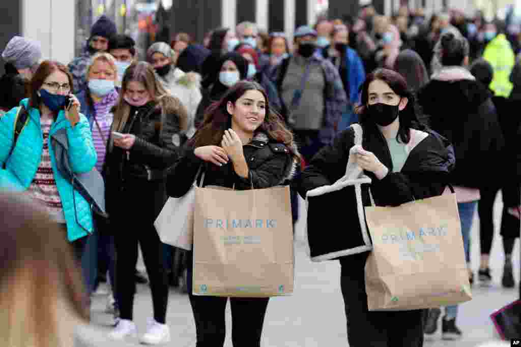 People carry shopping bags while others queue to enter a store on Oxford Street in London as the government takes the next step on its lockdown.