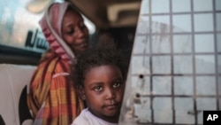 Seorang ibu dan anak perempuannya tengah menunggu bus di Izba, dekat Khartoum, Sudan, 14 Apri 2015. (Foto: dok).