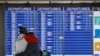 FILE - People embrace in front of a flight departures board at Dulles International Airport in Dulles, Va., March 17, 2020. At least 15 VOA journalists are to return to their country of origin in coming weeks, after USAGM did not renew their J-1 visas.