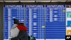 FILE - People embrace in front of a flight departures board at Dulles International Airport in Dulles, Va., March 17, 2020. At least 15 VOA journalists are to return to their country of origin in coming weeks, after USAGM did not renew their J-1 visas.