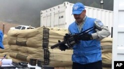 FILE - In this photo released by the United Nations mission based in Colombia, a member of U.N. monitoring mission for the Colombian peace process holds a weapon handed over by rebels of the Revolutionary Armed Forces of Colombia, FARC, in Buenos Aires in southern Colombia, June 13, 2017. 