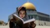 A girl sits with a holy book as the Dome of the Rock is seen in the background at the compound that houses al-Aqsa Mosque, known to Muslims as Noble Sanctuary and to Jews as Temple Mount, in Jerusalem's Old City.