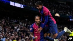 Raphinha celebra com Lamine Yamal, depois de marcar o quarto golo da sua equipa durante o jogo da La Liga, contra o Real Madrid no estádio Santiago Bernabeu em Madrid, Espanha, sábado, 26 de outubro de 2024.