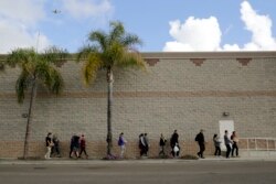 FILE - Volunteers carry donated items towards a group of undocumented migrants looking for work as day laborers alongside a hardware store in San Diego, California, Feb. 4, 2017.