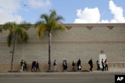 FILE - Volunteers carry donated items towards a group of undocumented migrants looking for work as day laborers alongside a hardware store in San Diego, California, Feb. 4, 2017.