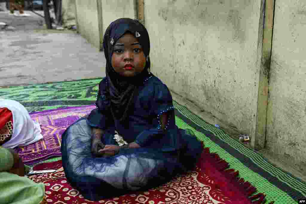 A young girl sits on a mat, as worshippers arrive to pray to mark the Muslim Eid-al-Adha, in Kara, Ogun State in southwest Nigeria.