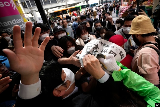 An employee distributes extra editions of the Yomiuri Shimbun newspaper reporting on Japan's victory at the final match of the World Baseball Classic Wednesday, March 22, 2023, in Tokyo. The headline of the newspaper said "Japan is No. 1 in the World." (AP Photo/Eugene Hoshiko)