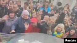 Gambar yang diambil dari rekaman video menunjukkan kerumunan warga bersorak dan berjabat tangan dengan tentara Ukraina di dalam mobil di Lapangan Kemerdekaan Kherson hari Jumat (11/11). 