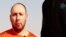 An image grab taken from a video released by the Islamic State (IS) and identified by private terrorism monitor SITE Intelligence Group purportedly shows U.S. freelance writer Steven Sotloff dressed in orange and on his knees in a desert landscape speaking to the camera before being beheaded by a masked militant (R), Sept. 2, 2014. 