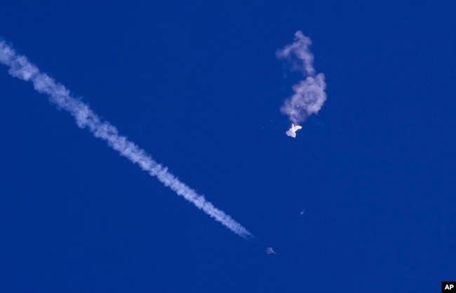 资料照：在美国南卡罗莱纳州海岸被美军击落的中国间谍气球残余物漂浮在空中，下方是美军战斗机和它的尾迹。（2023年2月4日）