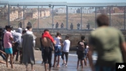 FILE: Spanish security forces stand guard as Moroccan and Sub-Saharan migrants gather at the border of the Spanish enclave of Ceuta, on Wednesday, May 19, 2021. 