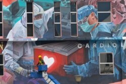 FILE - A worker adds finishing touches to giant mural tribute to frontline workers in the COVID-19 coronavirus pandemic outside a hospital in Kuala Lumpur, Malaysia, on Jan. 21, 2021.